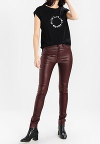Czarny t-shirt z krótkim rękawem z białym logo, zestawiony z burgundowymi spodniami z ekoskóry i czarnymi botkami na kostkę. Gładka faktura i dopasowany krój.