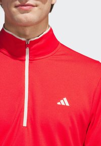 Red athletic quarter-zip pullover featuring a textured fabric, white zipper, and a small white logo on the chest.