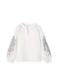 Blouse blanche à manches longues avec col en V ouvert, broderie florale noire sur les manches et surpiqûres noires près des épaules.