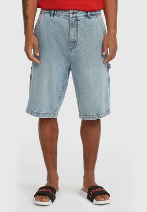 Svetlomodré denimové cargo šortky s bočnými vreckami, voľného strihu a ošúchaným lemom. Nosené s čiernymi šľapkami s červenými detailmi.