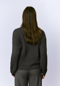 Suéter de punto grueso en gris oscuro con un corte holgado, mangas anchas y dobladillo acanalado, combinado con pantalones grises a juego.