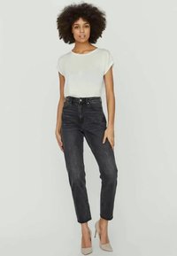 Top branco de manga curta combinado com jeans pretos de cintura alta. Os jeans têm um corte slim e uma perna ligeiramente afunilada, complementados com saltos nude.