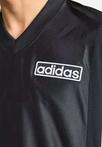 Camisa atlética preta com design em V. Apresenta um tecido suave, painéis em malha e um logo da Adidas bordado em branco no peito.