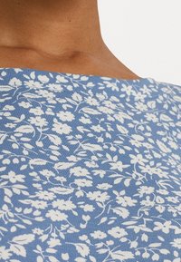 Blommönstrad topp med blå bakgrund som har vita blommor. Tyget har en slät yta och en rund halsringning.