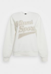 Vit sweatshirt med rundad halsringning och långa ärmar. Har en texturerad "Miami Sports"-tryck i beige över framsidan.
