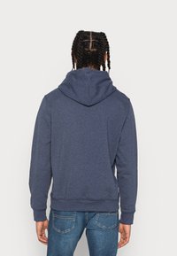Hoodie bleu marine avec poche kangourou, poignets et ourlet côtelés. Tissu doux, capuche avec cordon de serrage, coupe décontractée, vue arrière. Associé à un jean bleu.
