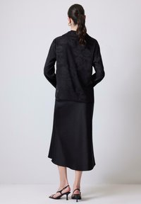 Camicia nera a maniche lunghe con texture floreale, abbinata a una gonna midi nera in satin elegante e tacchi neri con cinturino.