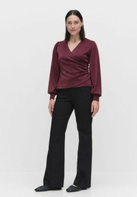 Burgundy wrap-top dengan lengan panjang yang mengembung. Warna solid dengan sedikit kilau, dipadukan dengan celana hitam mekar dan sepatu hitam datar.