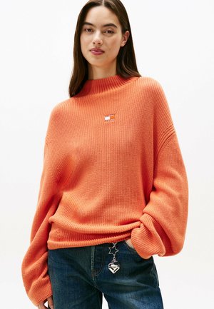 Gebreide oranje trui met een hoge halslijn, gezakte schouders en geribbelde textuur. Bevat een klein logo-opdruk en een relaxte pasvorm.