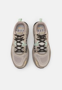 Baskets beige légères avec tige en maille texturée, lacets noirs et accents vert menthe. Présente le logo GORE-TEX et des détails à motifs.