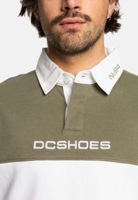 Zelená a bílá polo košile s texturovanou tkaninou, která má límec a vyšívané logo "DCSHOES" na přední straně.