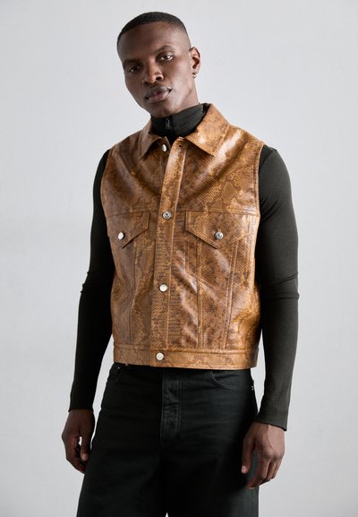 Brun slangeskindsprint lædervest med krave, frontlommer med trykknapper og en cropped design, parret med en tætsiddende sort langærmet top.