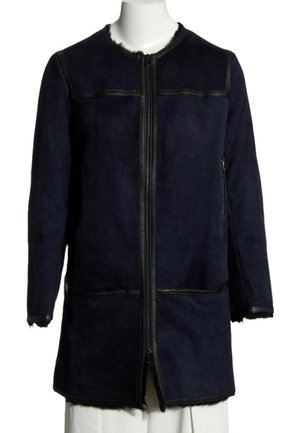 Veste longue bleu marine avec fermeture éclair à l'avant, garniture en cuir noir, manches longues et poche latérale zippée sur un mannequin blanc.