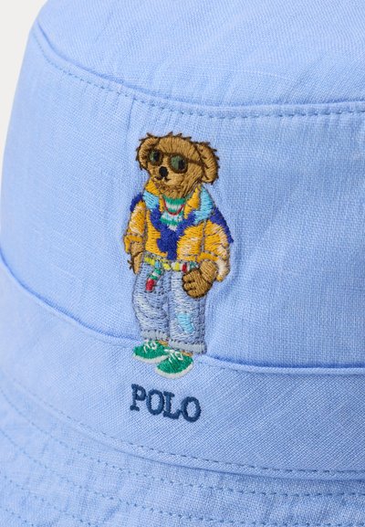 Ανοιχτό μπλε καπέλο-κουβάς από ύφασμα, με κεντημένη την εικόνα μιας αρκούδας σε casual ενδυμασία και το κείμενο "POLO" κεντημένο στο κάτω μέρος.