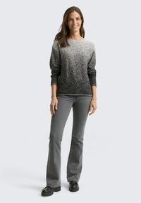 Grauer Gradient-Pullover mit langen Ärmeln und strukturierter Oberfläche. Kombiniert mit grauen Schlagjeans und schwarzen Plateauschuhen.