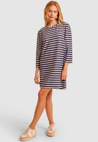 Pasiasta sukienka w kolorach granatowym i beżowym, wykonana z miękkiej tkaniny. Posiada okrągły dekolt oraz rękawy o trzy czwarte długości, w długości do kolan.