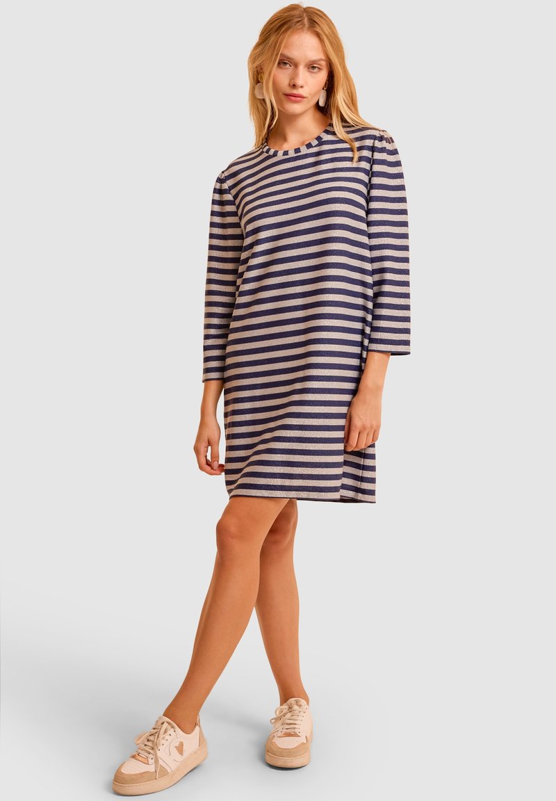 Pasiasta sukienka w kolorach granatowym i beżowym, wykonana z miękkiej tkaniny. Posiada okrągły dekolt oraz rękawy o trzy czwarte długości, w długości do kolan.