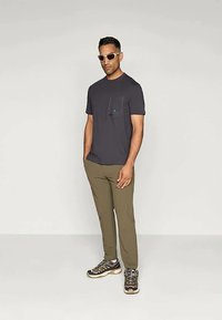 Dark gray short-sleeve t-shirt with a chest pocket, olive-green pants, and black shoes with beige accents. Model wears white sunglasses.