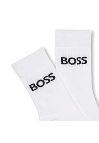 Vita ribbade strumpor med en svart "BOSS"-logotyp på sidan, som framhäver enkelhet i designen och kontrasterande färger.