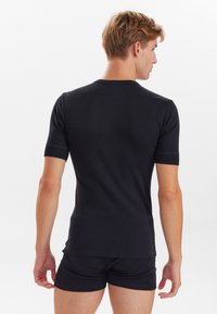 Sort kortærmet T-shirt i en tætsiddende design, med rund halsudskæring og blødt, strækbart stof. Bæres med matchende sorte shorts.