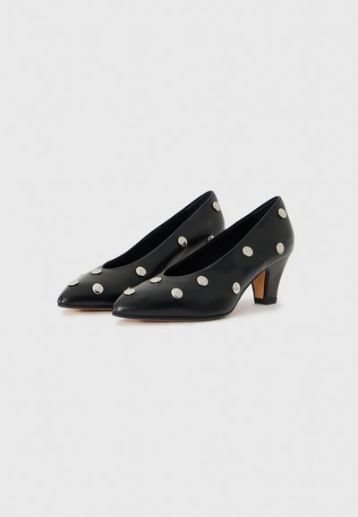 Black patent leather heels with a pointed toe, featuring large silver polka dot accents and a mid-height block heel.