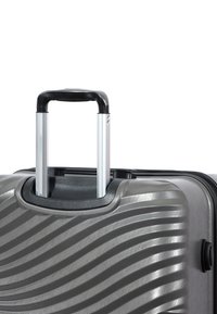 Silver hard-shell suitcase with a textured wave pattern, featuring a black retractable handle and zipper closure.