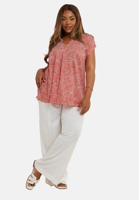 Blusa corta de manga corta con un patrón rojo y pliegues, combinada con pantalones de lino blancos sueltos y sandalias blancas.