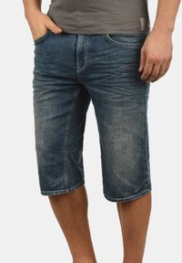 Shorts en denim bleu foncé avec une texture usée et décolorée. Comprend cinq poches, des passants de ceinture et un design droit se terminant juste au-dessus du genou.