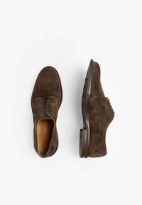 Zapatos de vestir de ante marrón con puntera redondeada, diseño de cordones con cinco ojales y suela de goma texturizada con pequeñas tachuelas para mayor agarre.