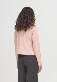 Lichtroze katoenmix jas met een cropped ontwerp, lange mouwen en een gladde textuur, gecombineerd met strakke donkergrijze broek.