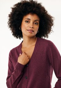 Burgundský cardigan vyrobený z měkké látky, s výstřihem do V, žebrovanými manžetami a se čtyřmi černými knoflíky vpředu.