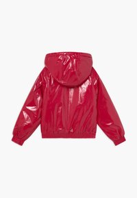 Giacca a pullover rossa e lucida con cappuccio. Presenta polsini e orlo elasticizzati, una texture liscia e un design minimalista senza tasche.