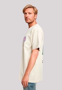 Light beige cotton t-shirt with short sleeves, featuring a round graphic patch on the front and colorful prints on the back.