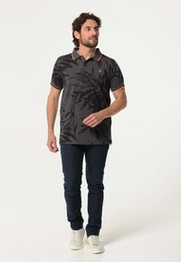 Polo shirt in donkergrijs met zwarte bladerenpatronen, contrasterende oranje kraag en mouwafwerkingen. Draag het met een donkere jeans en witte sneakers.