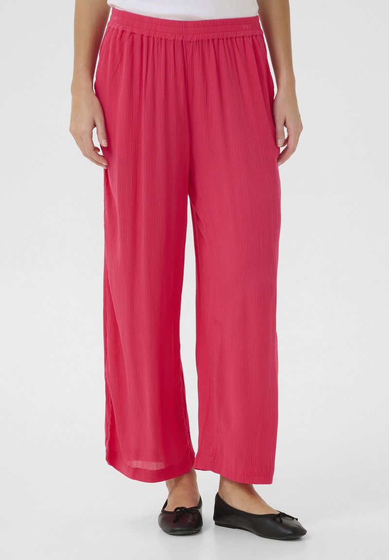 Pantalons légers à jambes larges en tissu rose vif avec une texture. Dotés d'une taille élastique, ils tombent confortablement jusqu'aux chevilles.