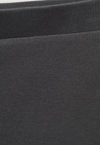 Crna rebrasta tkanina s glatkom teksturom i elastičnom gumicom, pogodna za udobno nošenje i svestranost u stiliziranju.