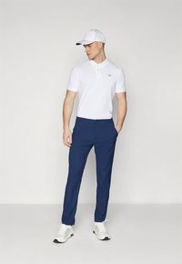 Biele polo tričko s krátkymi rukávmi, námornícke modré nohavice a biele tenisky. Oblečenie dopĺňa biela šiltovka.