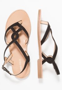 Mustat mokka-sandaalit, joissa on tasapohjat, ristiin menevällä hihnasuunnittelulla ja vaaleanruskealla sisäpohjalla. Säädettävä nilkkahihna ja pyöristetty kärki.