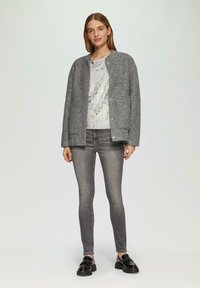 Szary, teksturowany kardigan nałożony na srebrną bluzkę z cekinami, w połączeniu z dopasowanymi szarymi jeansami i czarnymi platformami. Prosty, nowoczesny design.