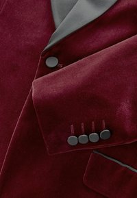 Burgundy bársonykabát szürke selyemgallérral, öt fekete, szövetbe burkolt gombbal az ujjak végén és kontrasztos zseb szegéllyel.