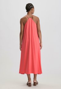 Maxi-mekko korallinvärisessä sävyssä, valmistettu pehmeästä kankaasta, jossa on halterneck-malli, virtaava muotoilu ja polven pituiset helmukset. Yhdistetty lohkopohjaisiin sandaaleihin.