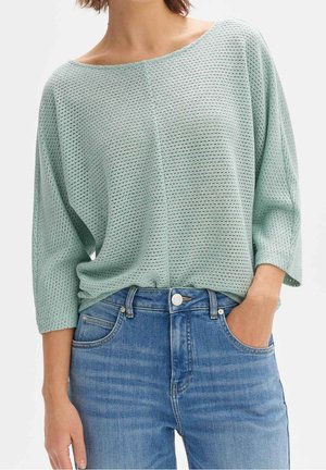 Top de punto verde menta claro con un ajuste holgado, escote ancho y mangas tres cuartos, combinado con vaqueros azules.