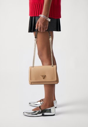 Beige strukturovaná kabelka s logem, řetízkem a strukturovaným povrchem. Nesená s červeným svetrem, plisovanou sukní a metalickými balerínami.