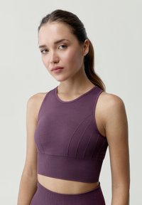 Fioletowa koszulka sportowa z teksturowanym, żebrowanym wzorem. Posiada okrągły dekolt oraz krótką sylwetkę. Materiał wydaje się gładki i dopasowany.