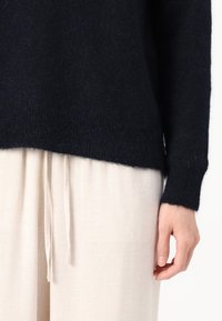 Navy wool sweater with soft texture and ribbed cuffs, paired with cream linen trousers featuring a drawstring waist and subtle texture.