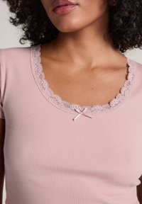Rosa ribbat t-shirt med en scalloped spetskrage och en liten rosettdetalj i mitten. Mjuk, figurnära design.