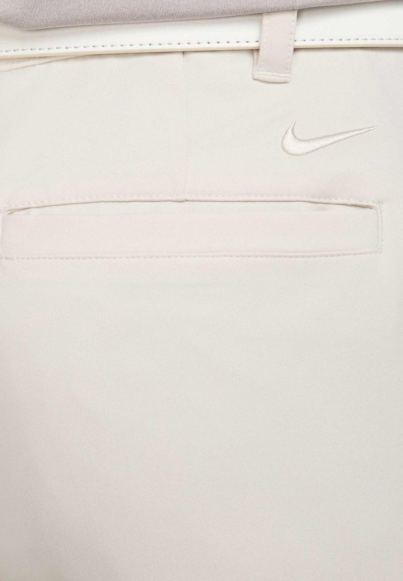 Nike bukser i lys beige stof med en glat tekstur. Har en baglomme og et broderet Nike-logo i en matchende nuance.