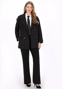 Fekete dupla soros ballonkabát vállrakattal, fehér inget és fekete nyakkendőt viselve. Vékony fekete nadrág és fekete magassarkú egészíti ki az öltözéket.