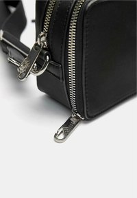 Borsa a tracolla nera in materiale sintetico con zip e accessori in argento, dotata di doppi cursori e di una forma rettangolare elegante.