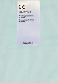 Vaaleansininen kangas, jossa on hieno verkko-textuuri, sisältäen valkoisen hoito-ohjelaput, joissa on turvallisuusohjeita ja CE-merkintöjä mustalla tekstillä.